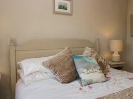 A bed with beige headboard white sheets two beige pillows one blue decorative pillow a bedside table with a lamp and framed picture on the wall at Holme Fell View in Sedbergh