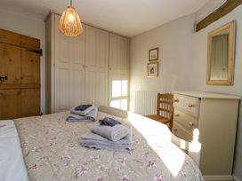 A bedroom with a bed covered in a floral quilt and folded towels a wooden door built in wardrobes a chair a chest of drawers and a mirror at Holme Fell View in Sedbergh