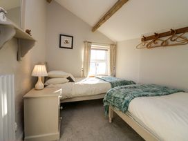 A bedroom with two single beds with green throws a nightstand with a lamp a window with curtains wooden hangers on the wall at Holme Fell View in Sedbergh