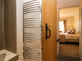 View from a bathroom with a shower and heated towel rail through a wooden door into a bedroom with a bed and window at Holme Fell View in Sedbergh