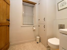 A bathroom with a toilet a wooden door a window with blinds a white cabinet and a small trash can at Holme Fell View in Sedbergh