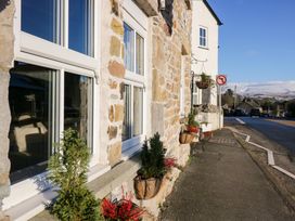A stone house facade with windows flower pots and a sidewalk along a street with a no left turn sign