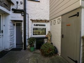 An outdoor corner with white stone walls two doors potted plants a statue and a window at Holme Fell View in Sedbergh