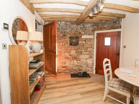 An entryway with a wooden door stone wall bookshelf with a lamp and a round mirror a wooden dining table with chairs at Holme Fell View in Sedbergh