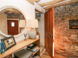A hallway with an open wooden door stone wall a wooden shelf with a lamp mirror and framed picture at Holme Fell View in Sedbergh