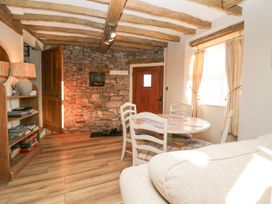 A room with wooden beams on the ceiling a stone wall a small round dining table with four chairs a bookshelf with a lamp and books and a beige sofa at Holme Fell View in Sedbergh