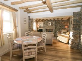 A dining area with a round wooden table and four chairs next to a living room with sofas and stone walls at Holme Fell View in Sedbergh