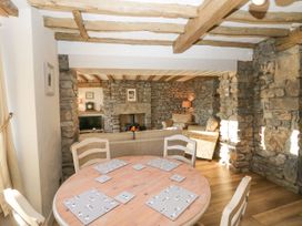 A dining area with a round wooden table and four chairs next to a living room with sofas and a wood burning stove at Holme Fell View in Sedbergh