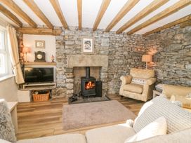 A living room with stone walls a wood burning stove armchairs a television and wooden ceiling beams at Holme Fell View in Sedbergh