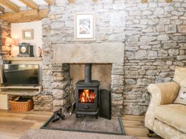 A living room with a stone fireplace wood burning stove a television on a stand a basket under the stand and a beige armchair at Holme Fell View in Sedbergh