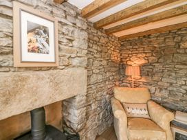 A stone wall corner with a framed picture of sheep a beige armchair with a sheep cushion and a floor lamp at Holme Fell View in Sedbergh