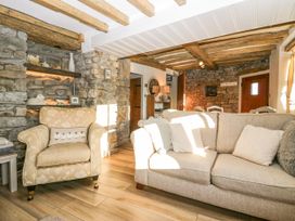 A living room with a stone wall a beige armchair and a sofa with cushions at Holme Fell View in Sedbergh