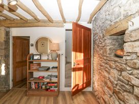 A hallway with a stone wall wooden ceiling beams a wooden bookshelf with books and a lamp and an open wooden door at Holme Fell View in Sedbergh
