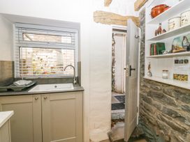 A kitchen sink below a window with blinds and shelves with jars and decorations next to a door with stone walls at Holme Fell View in Sedbergh
