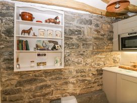 A kitchen corner with stone walls a white shelf holding containers and figurines and grey cupboards with a built in microwave at Holme Fell View in Sedbergh