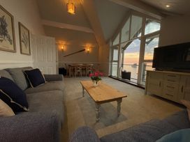 A living room with two sofas a wooden coffee table with flowers a dining table in the back and large windows overlooking water at 12 Thurlestone Rock in Thurlestone