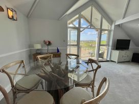 A dining area with a round glass table and six chairs near large windows and a door leading outside at 12 Thurlestone Rock in Thurlestone