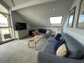 A living room with blue sofas a wooden coffee table with flowers a television and skylight window at 12 Thurlestone Rock in Thurlestone