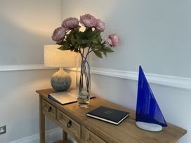 A wooden console table with a lamp a vase of flowers a guest book and a blue glass sailboat at 12 Thurlestone Rock in Thurlestone