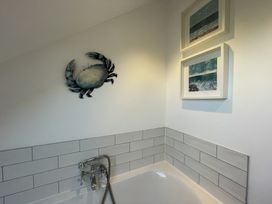 A bathroom corner with a bathtub faucet metal crab wall decoration and two framed ocean pictures at 12 Thurlestone Rock in Thurlestone