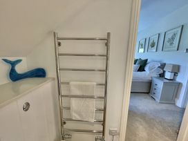 A bathroom with a towel rack and a blue whale decoration next to a doorway showing a bedroom with a bed and framed pictures on the wall at 12 Thurlestone Rock in Thurlestone