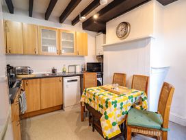 A kitchen with wooden cabinets a dining table covered with a colorful tablecloth and chairs at The Courtyard Cottage in Llangollen