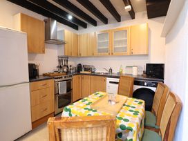 A kitchen with wooden cabinets a dining table with chairs and appliances at The Courtyard Cottage in Llangollen