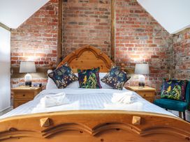 A bedroom with a wooden double bed white linens floral cushions bedside tables and lamps against a brick wall at The Courtyard Cottage in Llangollen