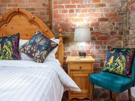 A bedroom with a wooden bed frame white bedding floral patterned pillows a wooden nightstand with a lamp and a teal chair with a floral pillow at The Courtyard Cottage in Llangollen