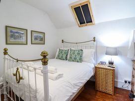 A bedroom with a white iron bed with green patterned pillows and folded towels a bedside table with a lamp and clock under a skylight at The Courtyard Cottage in Llangollen