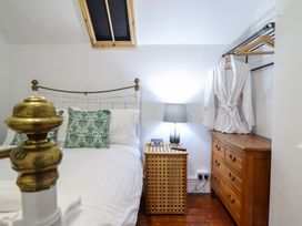 A bedroom with a white bed with green patterned pillows a wooden nightstand with a lamp and clock a wooden dresser with a white bathrobe hanging above at The Courtyard Cottage in Llangollen