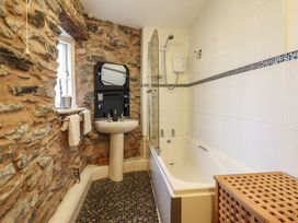 A bathroom with a stone wall, a pedestal sink, a bathtub with shower, a window, and a wooden laundry basket at The Courtyard Cottage in Llangollen