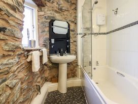 A bathroom with a stone wall a pedestal sink a bathtub with shower and a window at The Courtyard Cottage in Llangollen