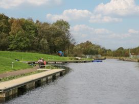 A river with a wooden dock and grassy bank with people fishing and trees in the background at Willow in Denny