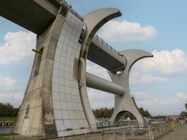 A large mechanical structure with curved supports and a horizontal arm by a riverbank