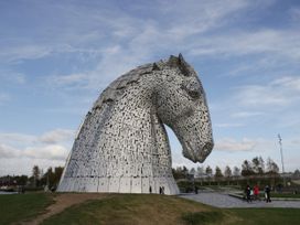 A large metal sculpture of a horse head outdoors with people walking nearby at Willow in Denny