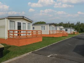 A row of mobile homes with wooden decks along a paved road in a grassy area at Willow in Denny