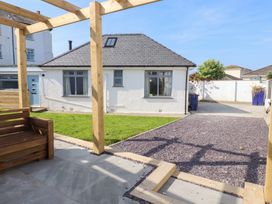 A backyard with a wooden pergola and seating area a gravel path a green lawn and a white house at Trearddur House Cottage in Trearddur Bay