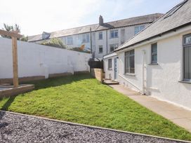 A backyard with green grass a stone pathway wooden fencing and white buildings at Trearddur House Cottage in Trearddur Bay