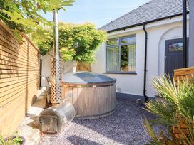 An outdoor space with a wooden hot tub and a metal stove next to a white house with a window and door at Trearddur House Cottage in Trearddur Bay