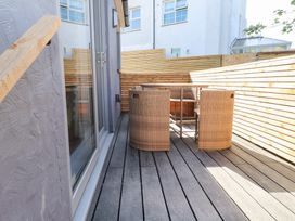 A wooden decked balcony with a glass door and a table with four wicker chairs at Trearddur House Cottage in Trearddur Bay