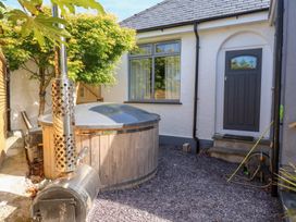 A small outdoor patio area with a covered wooden hot tub a tree a gray door and a window at Trearddur House Cottage in Trearddur Bay