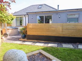 A backyard with a wooden fence hot tub potted plants and a grass lawn at Trearddur House Cottage in Trearddur Bay