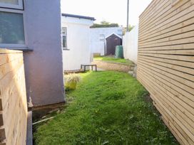 A narrow backyard with grass a wooden fence a small shed a flower pot and a compost bin at Trearddur House Cottage in Trearddur Bay