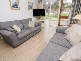 A living room with two gray sofas a television on a stand flowers on the stand and a sliding glass door showing a garden outside at Forbes C1 in Yarmouth