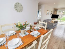 A dining table set with plates and glasses a vase with flowers a clock on the wall and a living area with a sofa and TV at Forbes C1 in Yarmouth