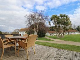 An outdoor wooden deck with a table and four wicker chairs overlooking a grassy area with palm trees and houses at Forbes C1 in Yarmouth