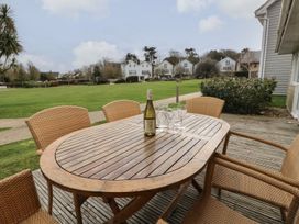 An outdoor wooden table with a bottle and glasses surrounded by wicker chairs on a deck at Forbes C1 in Yarmouth