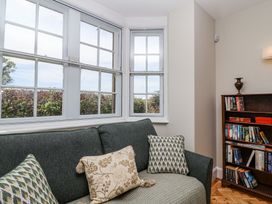 A corner of a living room with a dark green sofa with patterned cushions and a wooden bookshelf filled with books near a window at Middle Lodge near Taunton
