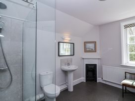 A bathroom with a shower, toilet, sink, mirror, small fireplace, radiator, and a chair near a window at Middle Lodge near Taunton